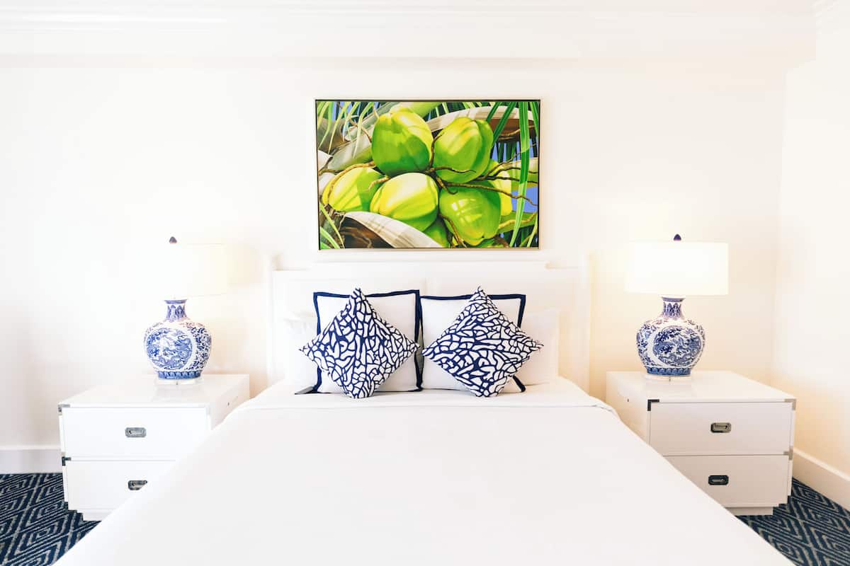 Une chambre d’hôtel avec un lit, deux tables de chevet, un vase sur chaque table de chevet et un tableau au-dessus du lit.