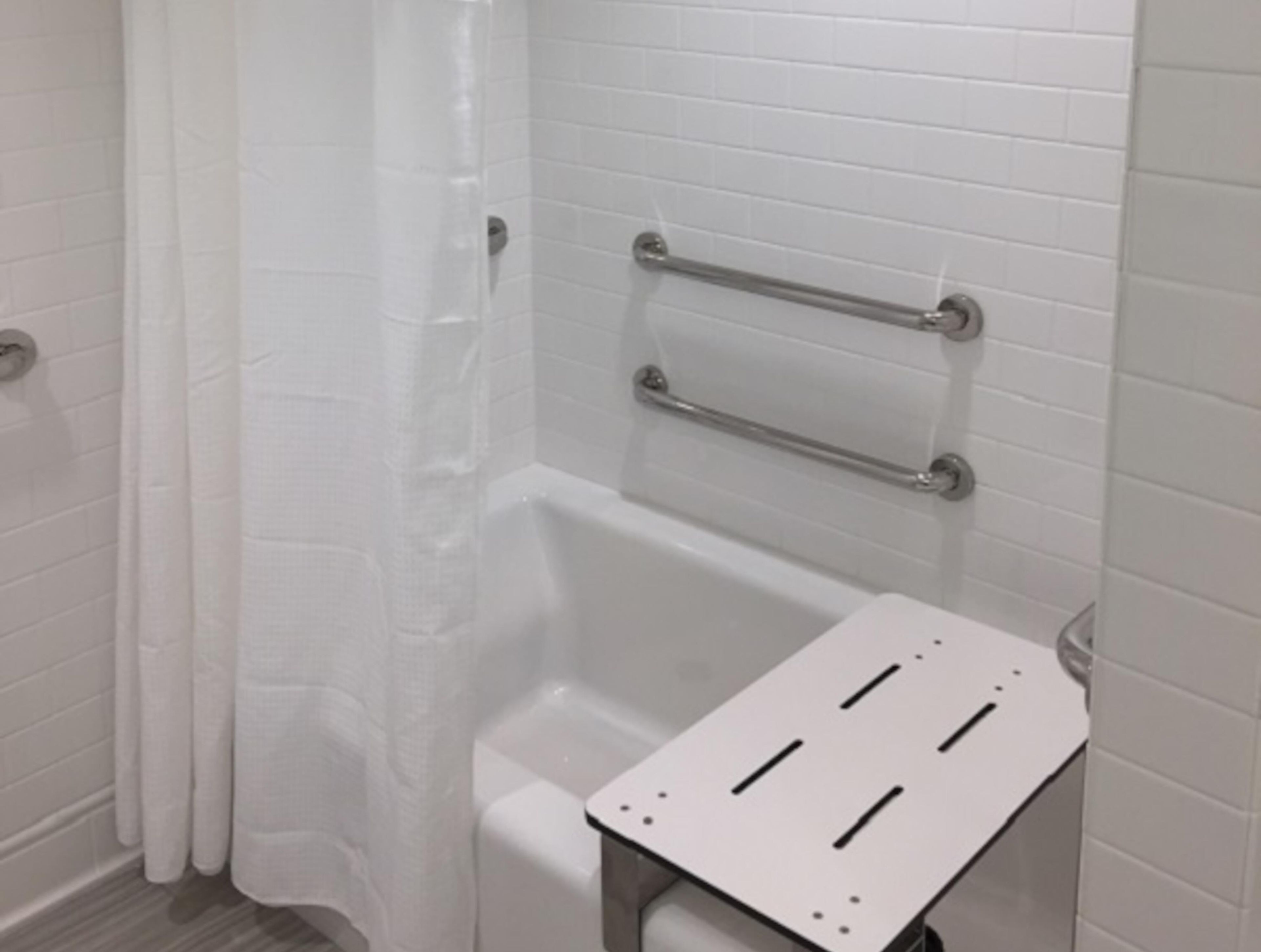 A bathroom with white tiled walls, a shower with a curtain, and a grab bar installed above the bathtub.