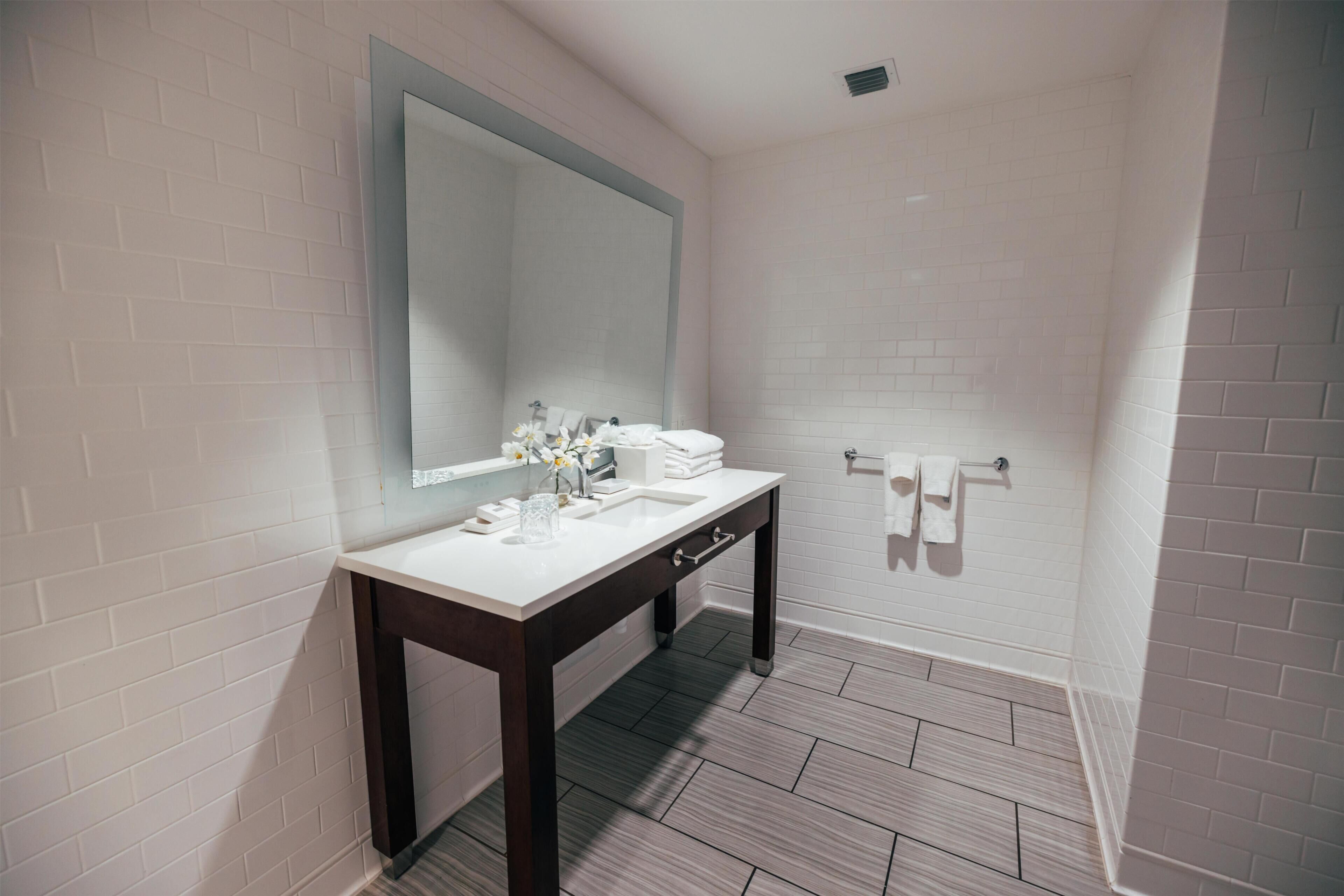 A bathroom with a white tiled wall, a large mirror, a white sink, and a wooden vanity.