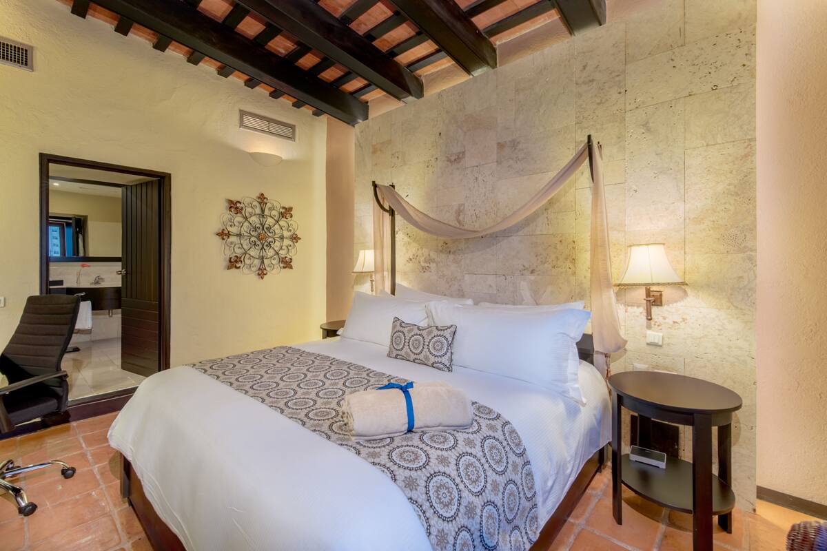 Una habitación de hotel con una cama grande, una silla, una mesita y una lámpara de pared.