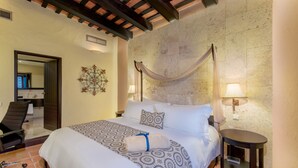 A hotel room with a large bed, a chair, a small table, and a wall-mounted lamp.