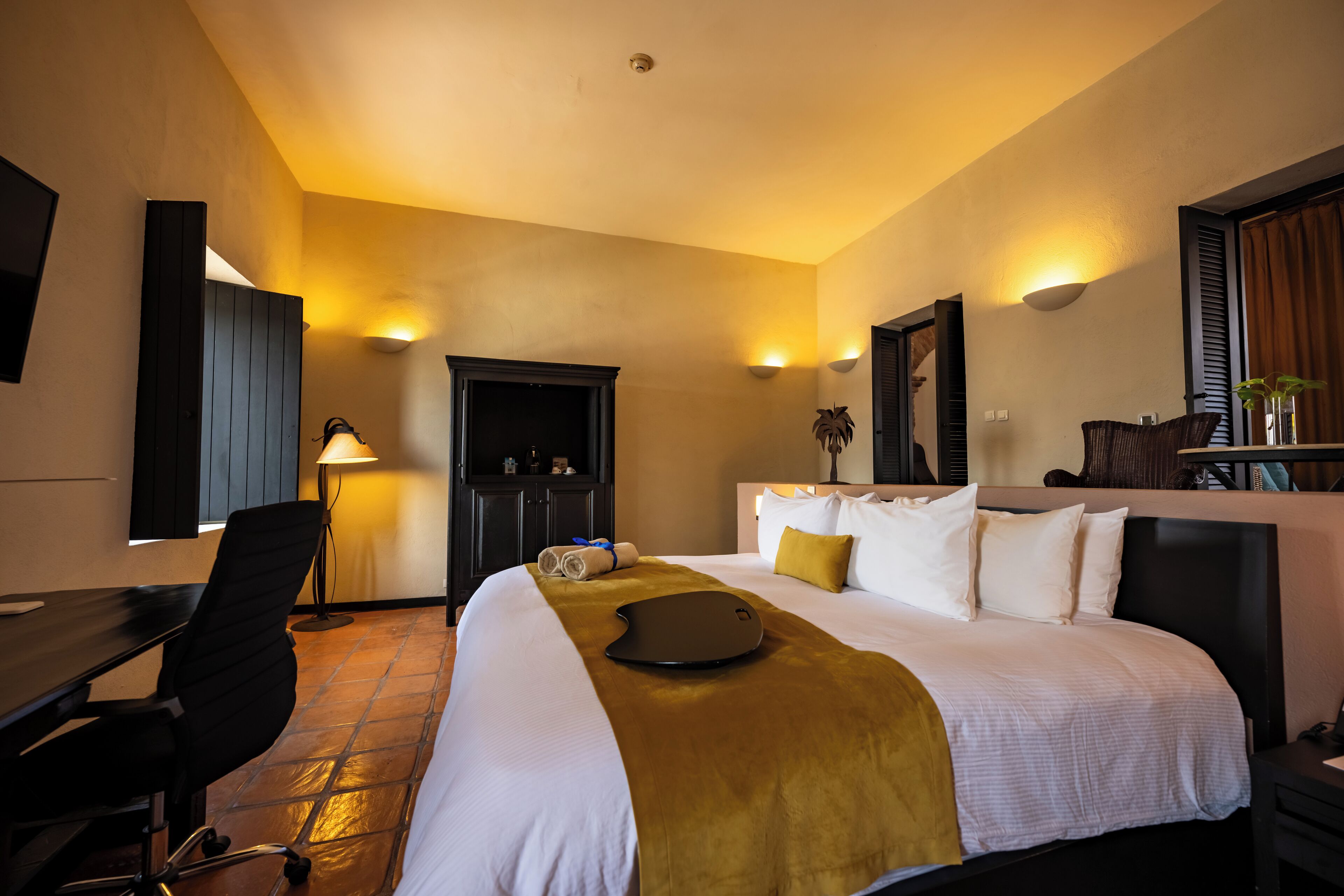Quarto de hotel com cama, escrivaninha, cadeira e abajur.