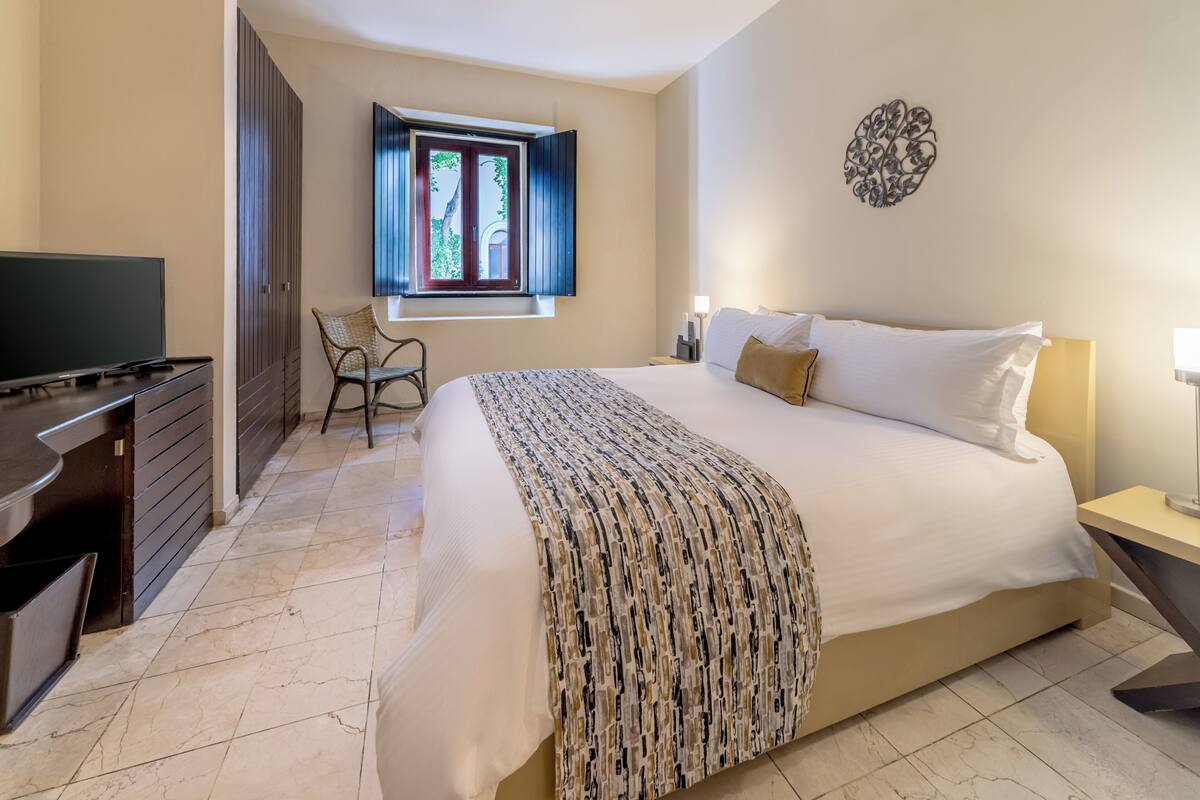 Una habitación de hotel con una cama, un televisor, un escritorio y una silla.
