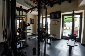 A gym with weightlifting equipment, a bench, and a window with a view of a pool. - Hodelpa Nicolas de Ovando (Santo Domingo)