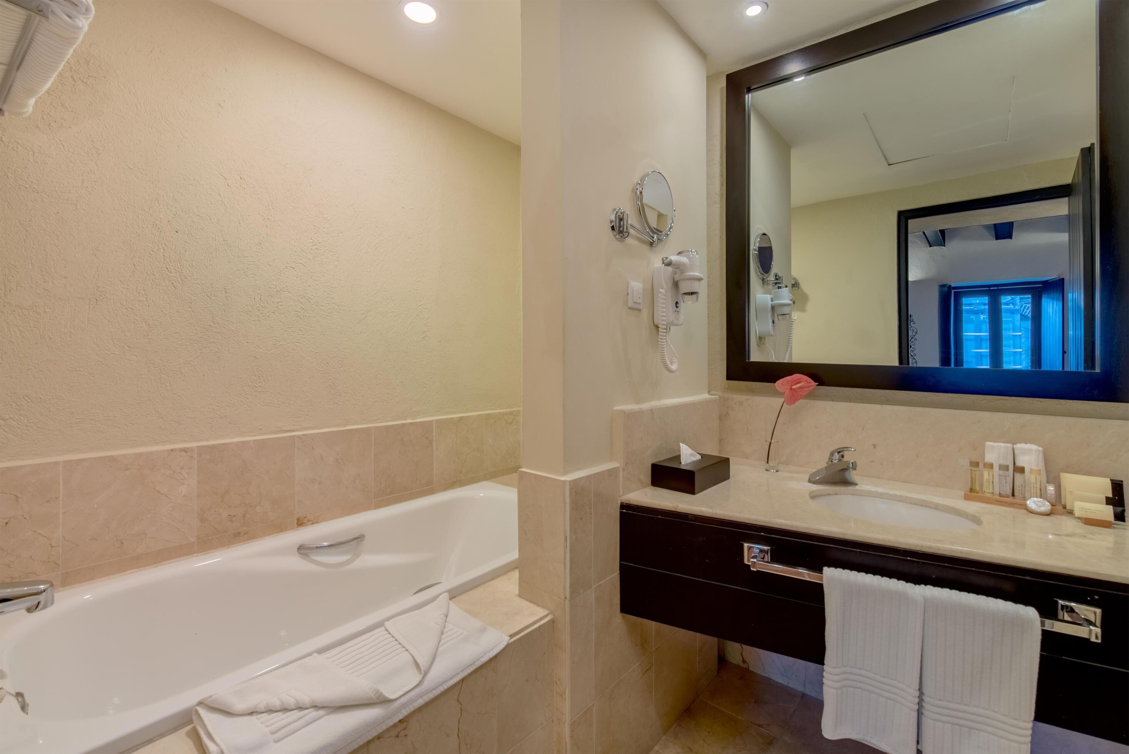 Un baño moderno con bañera, un espejo grande, tocador con lavamanos y artículos de aseo.