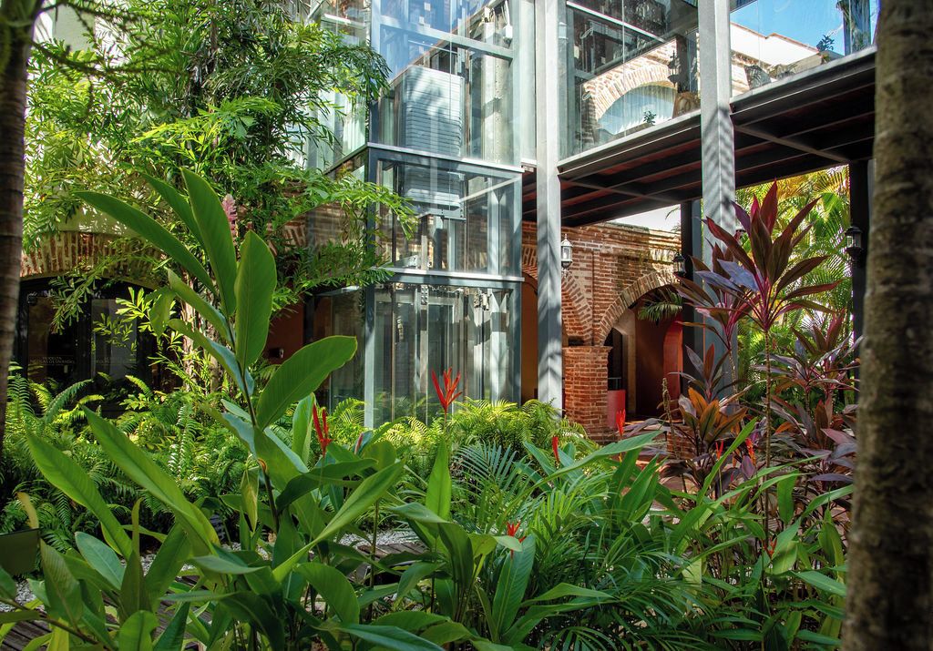 Un bâtiment moderne à l’architecture de verre et de brique, entouré d’une végétation luxuriante et de plantes tropicales.