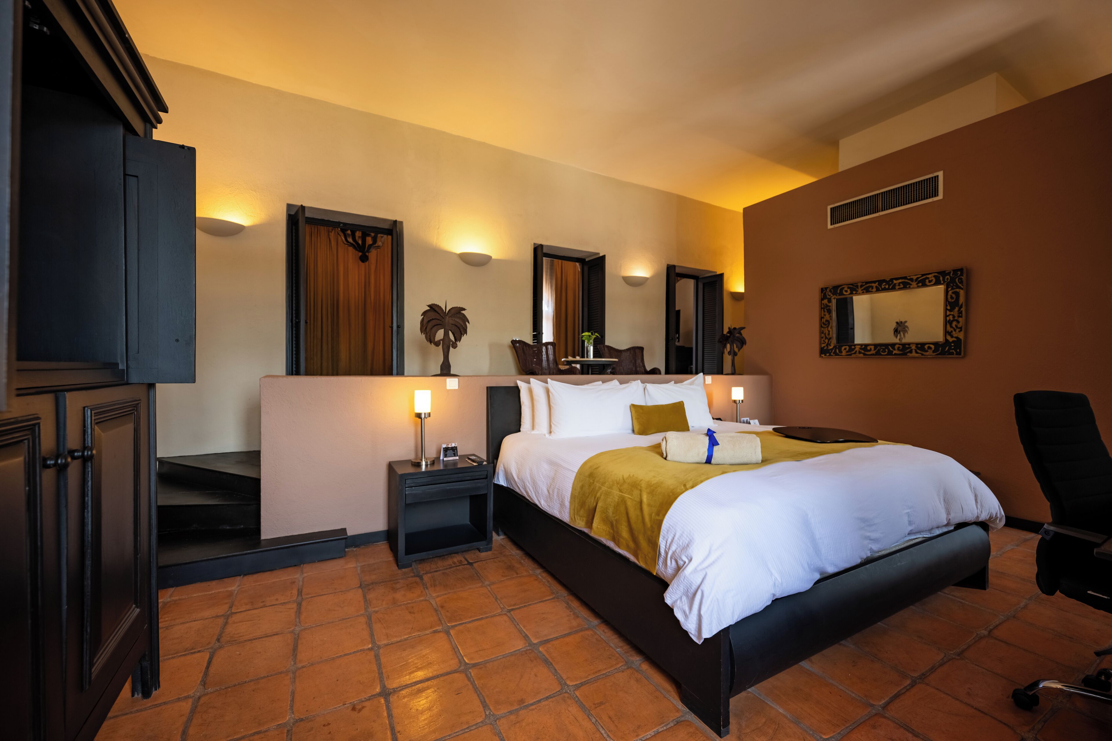 A hotel room with a large bed, two bedside tables, a desk, a chair, and a mirror on the wall.
