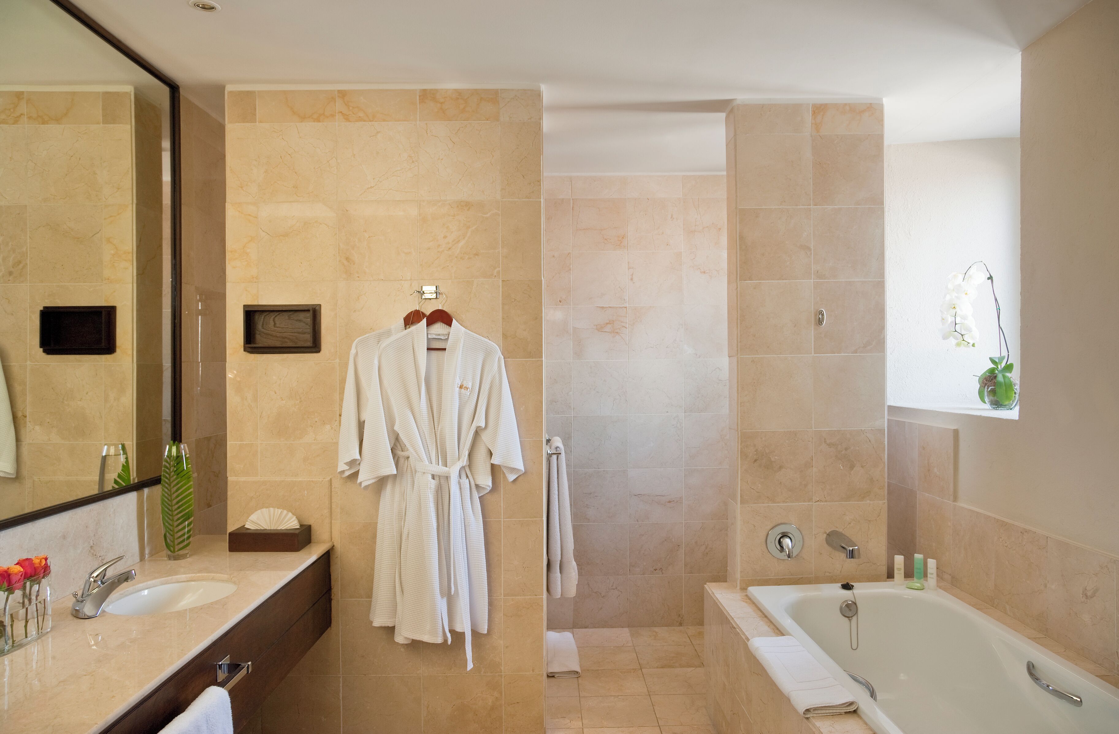 A modern bathroom with a large mirror, two sinks, a bathtub, and a walk-in shower.