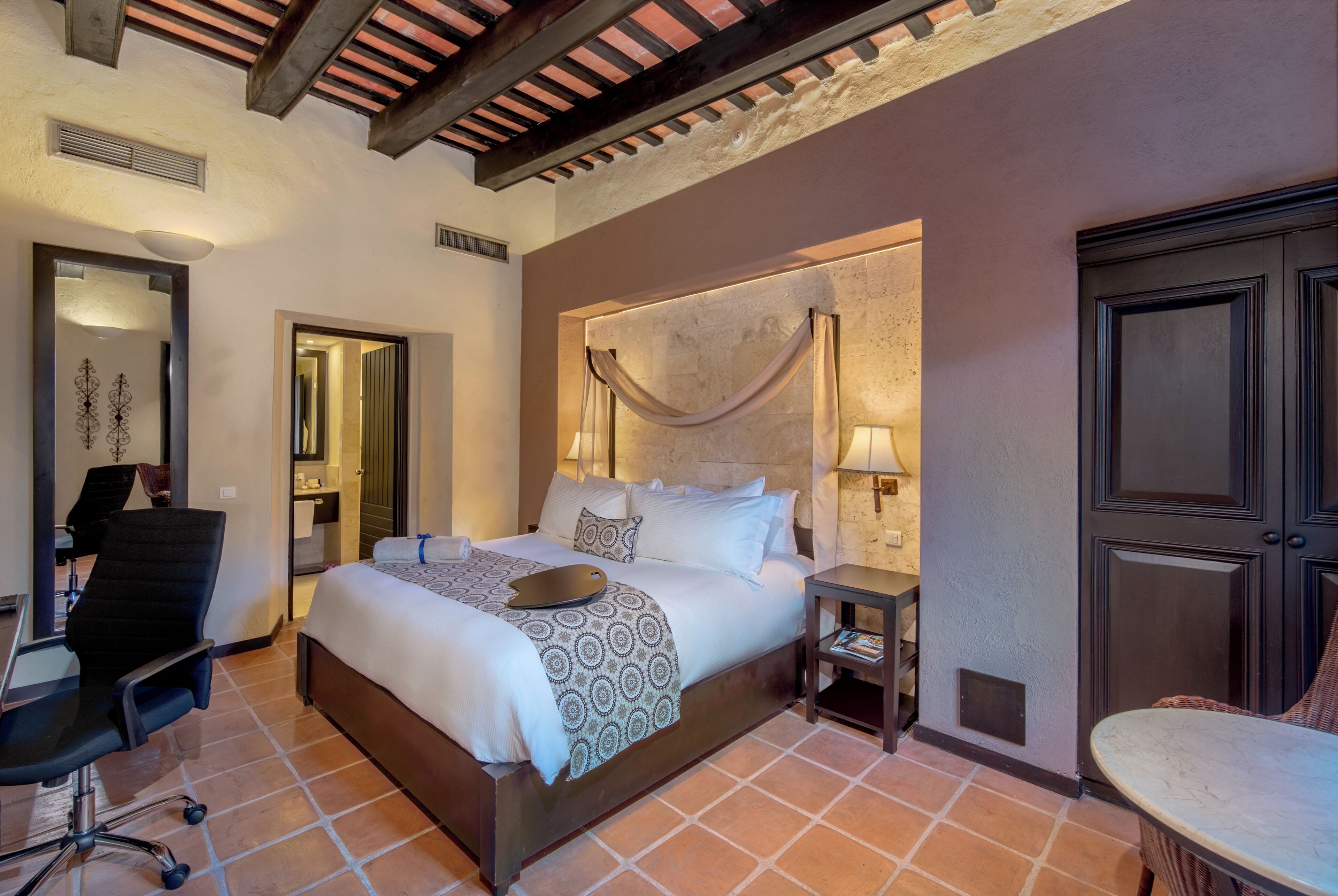 A bedroom with a large bed, a desk, a chair, and a small table.