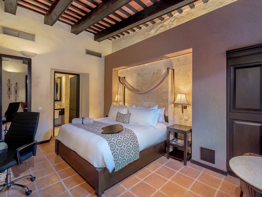 A bedroom with a large bed, a desk, a chair, and a small table.