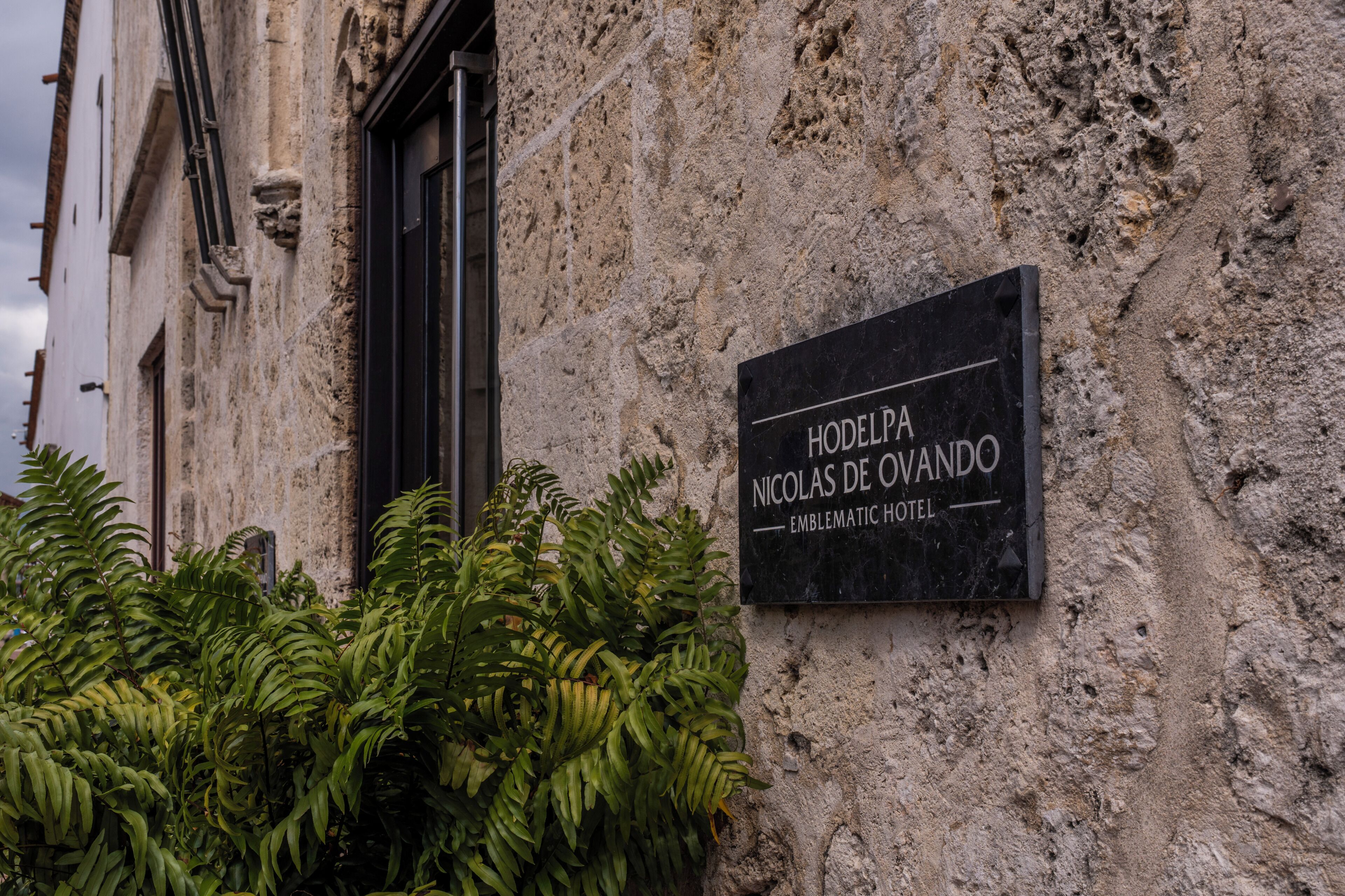 A sign for the 'Hodelpa Nicolas de Ocampo Emblematic Hotel' mounted on a stone wall.