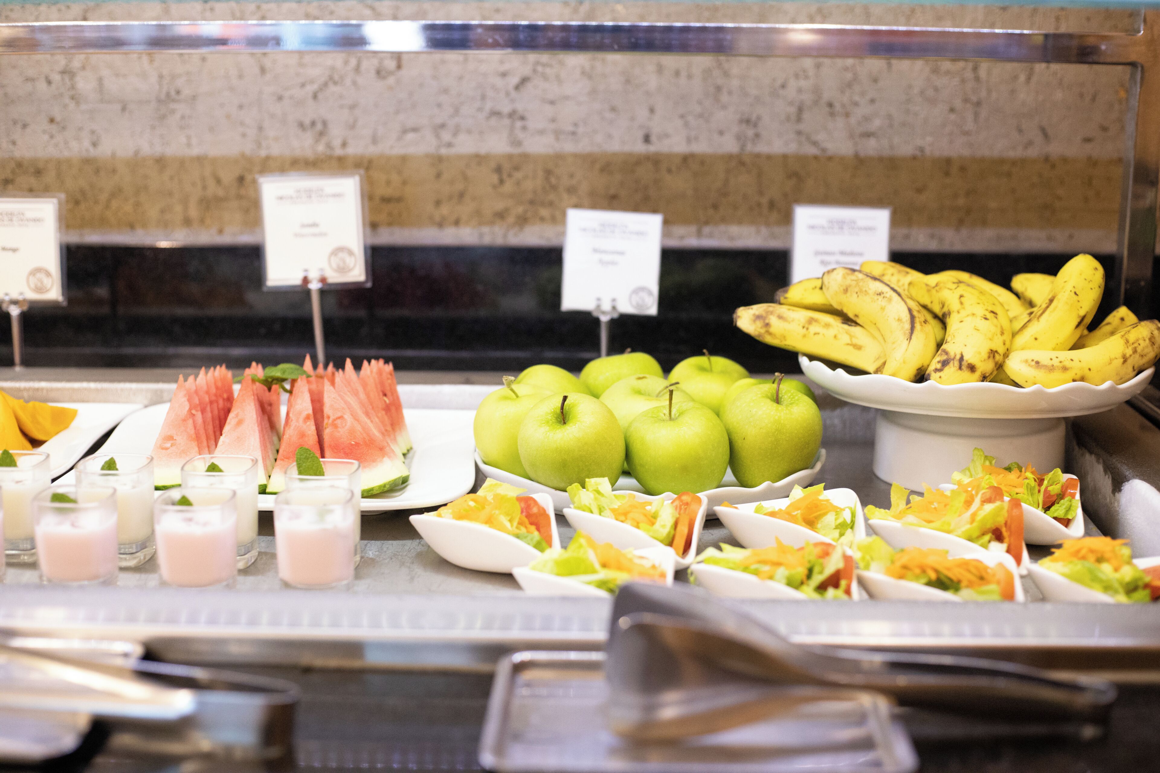 Een buffet met diverse gerechten, waaronder appels, bananen en salades.