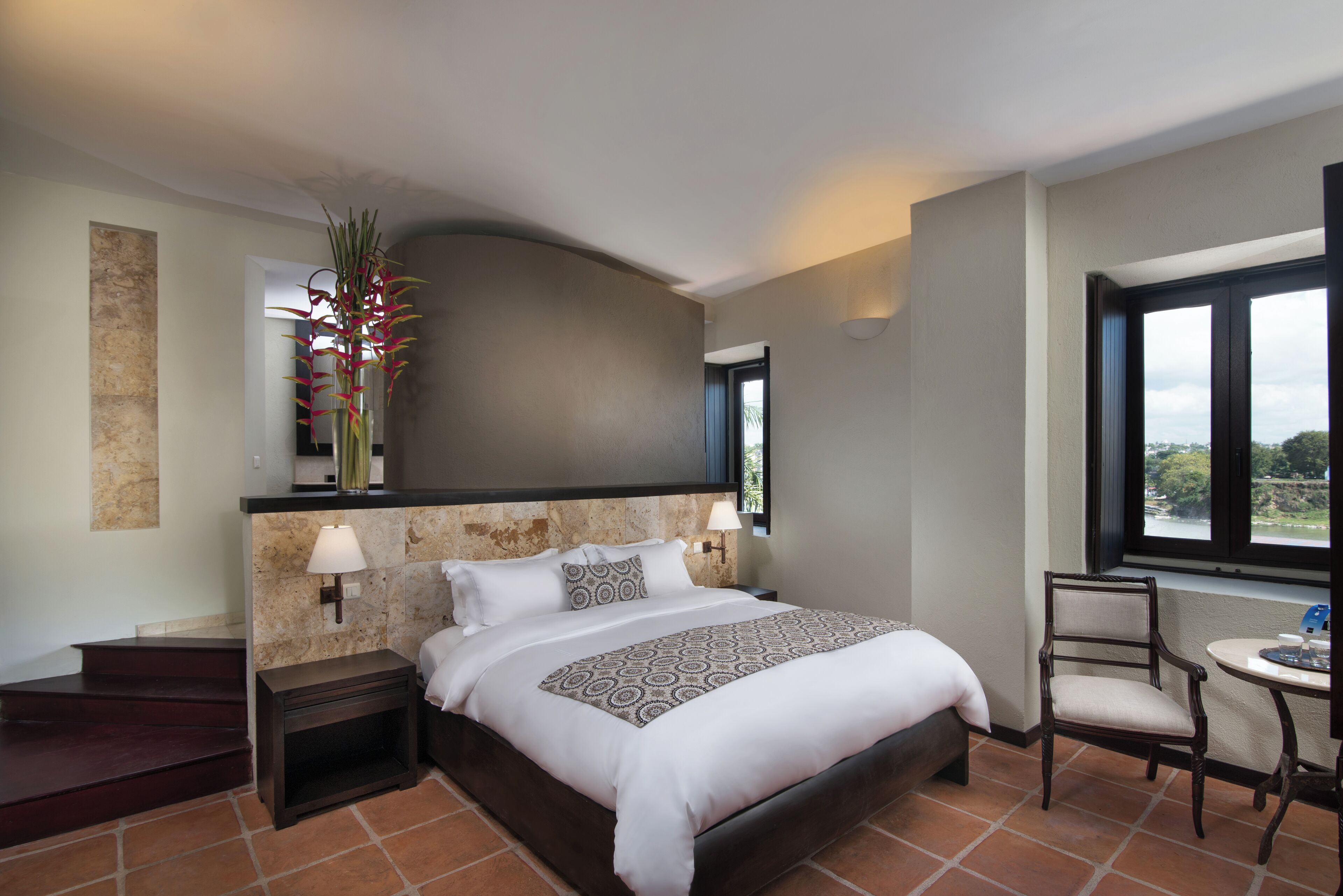 Habitación de hotel moderna con una cama grande, una mesita, una silla y vistas al exterior a través de una ventana.