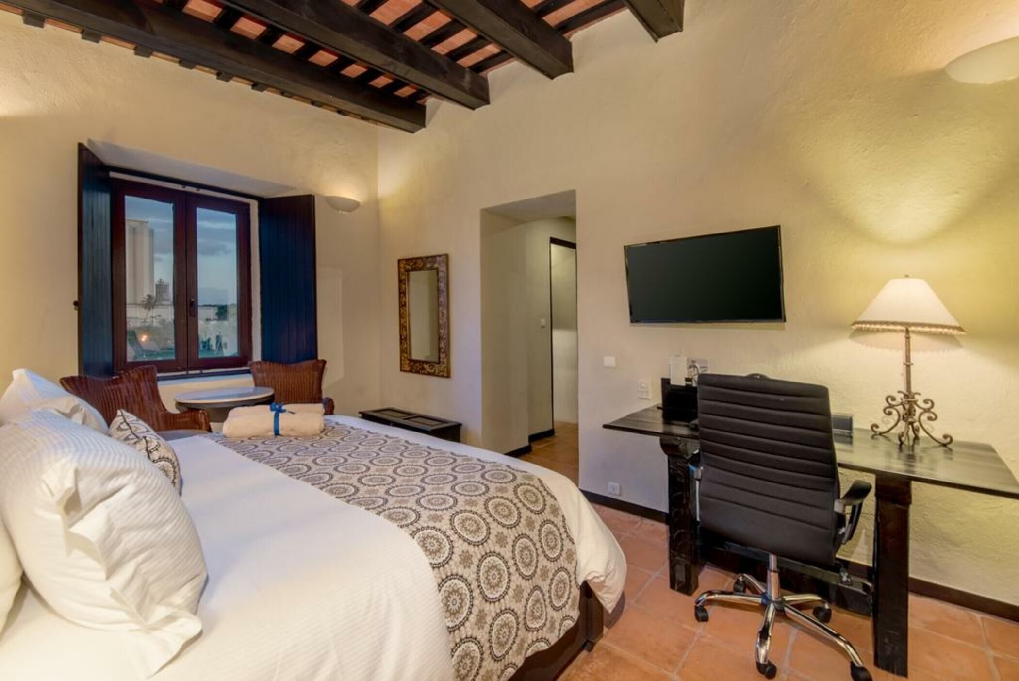A hotel room with a bed, a desk, a chair, a TV, and a window with a view.