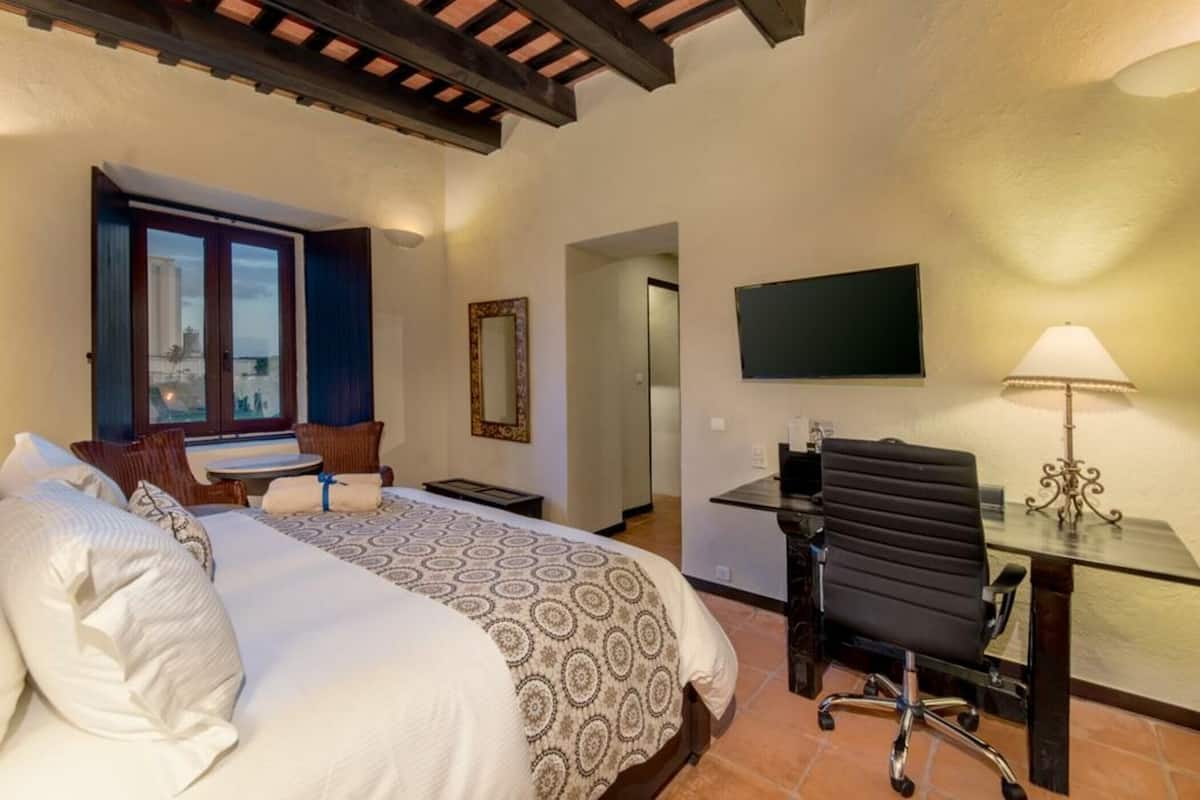A hotel room with a bed, a desk, a chair, a TV, and a window with a view.