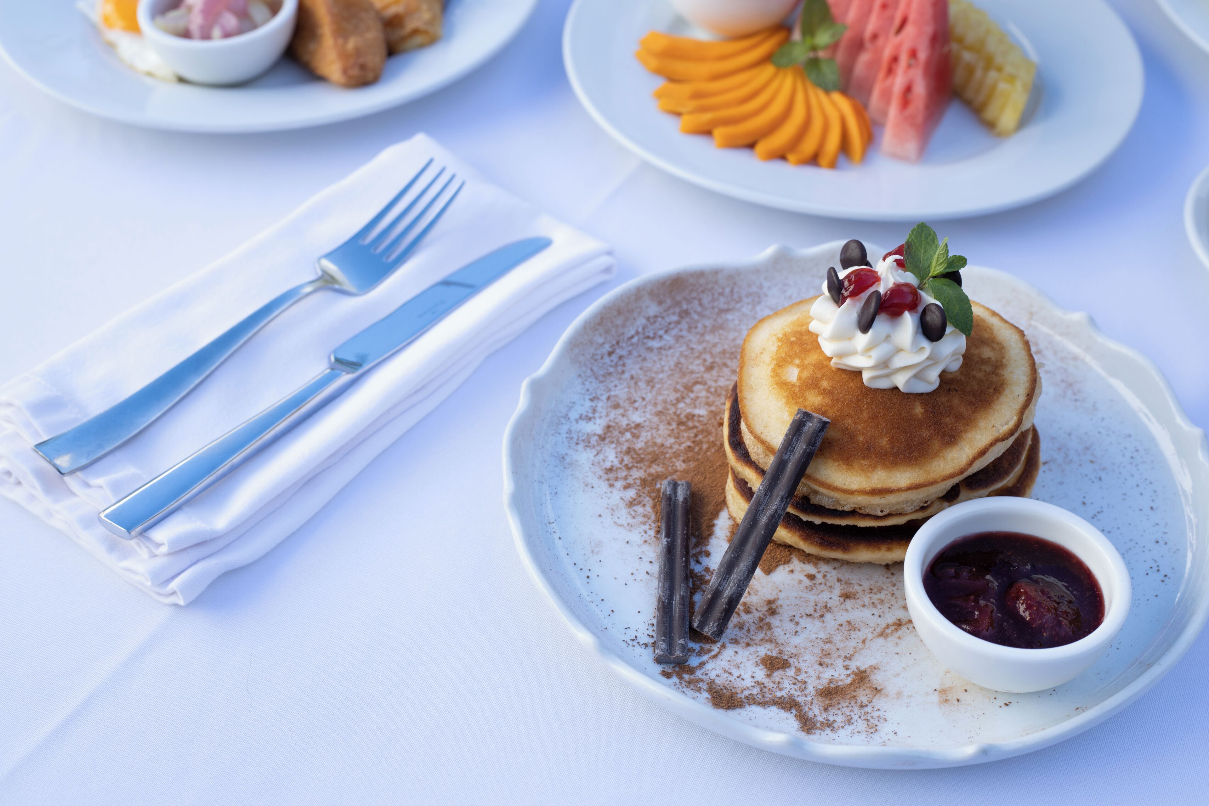 Ein Frühstückstisch mit Pfannkuchen, Beeren und einer kleinen Schale Marmelade.