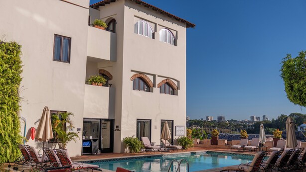 A poolside area with lounge chairs, a pool, and a building with balconies.