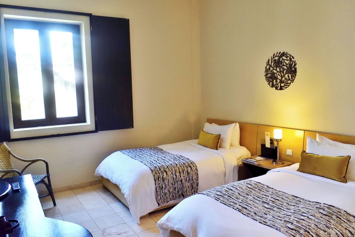 Habitación de hotel con dos camas, una silla, una mesa y un ventanal.