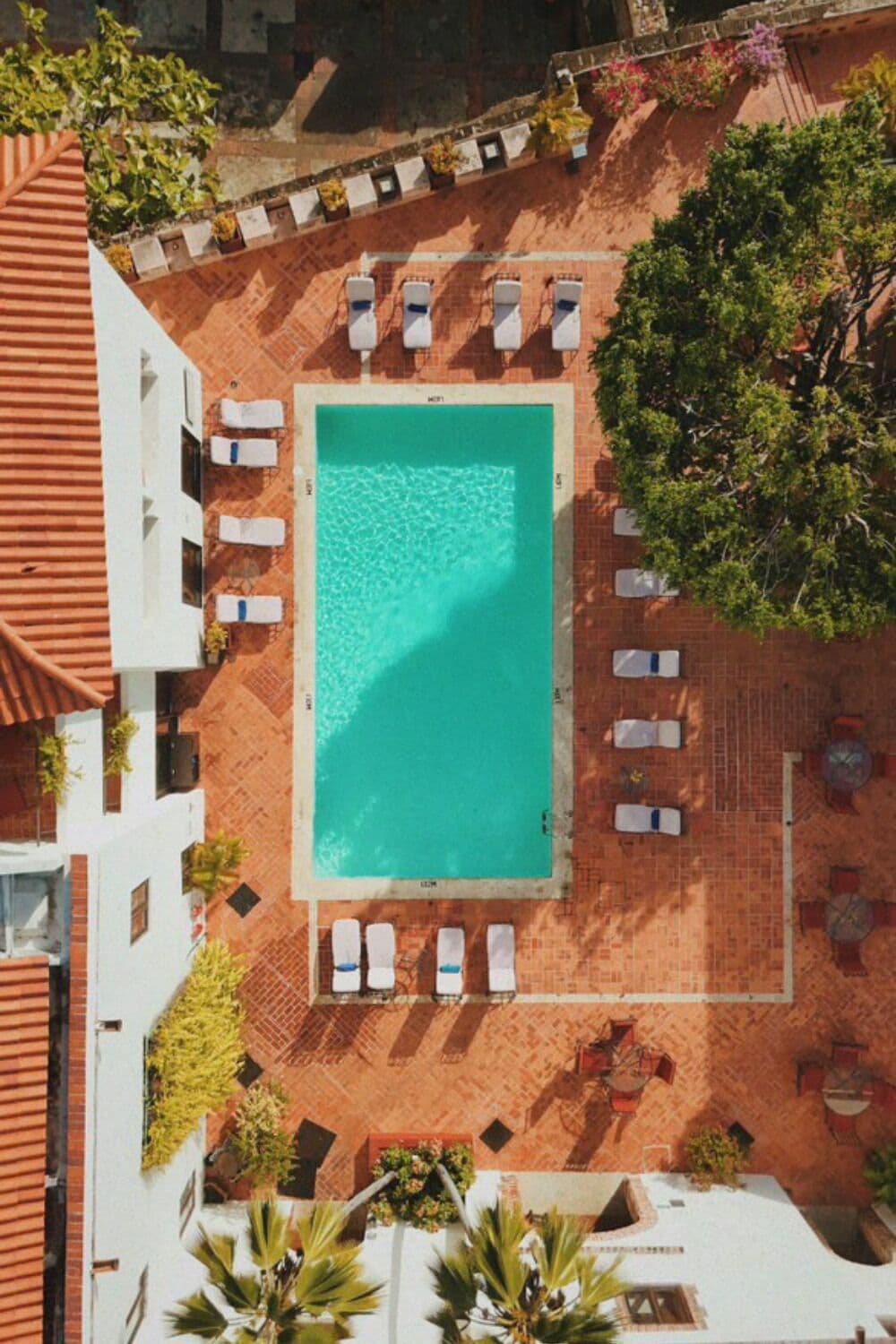 An aerial view of a rooftop pool area with a rectangular pool, surrounded by lounge chairs and potted plants.