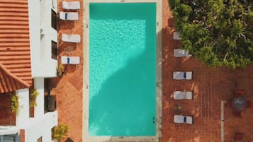 An aerial view of a rooftop pool area with a rectangular pool, surrounded by lounge chairs and potted plants.