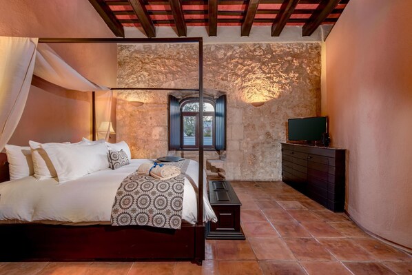 A bedroom with a bed, a TV, a dresser, and a stone wall.