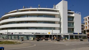A multi-story building with a curved facade, featuring a cafe and pizzeria on the ground floor. - Apartamento Ancora (Tossa de Mar)