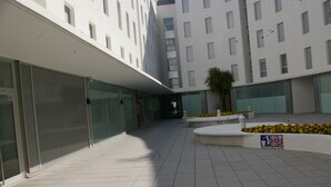 A modern building with a tiled courtyard, glass doors, and a planter with yellow flowers. - Apartamento Ancora (Tossa de Mar)