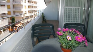 A balcony with two chairs, a table, and a potted plant with pink flowers. - Apartamento Ancora (Tossa de Mar)