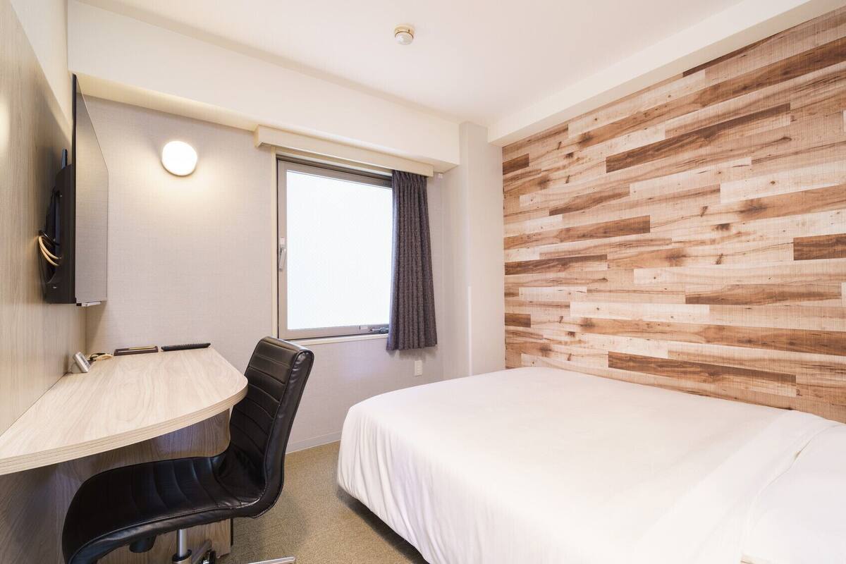 Une chambre d’hôtel comprenant un lit, un bureau, une chaise, une fenêtre avec des rideaux et un panneau mural en bois.