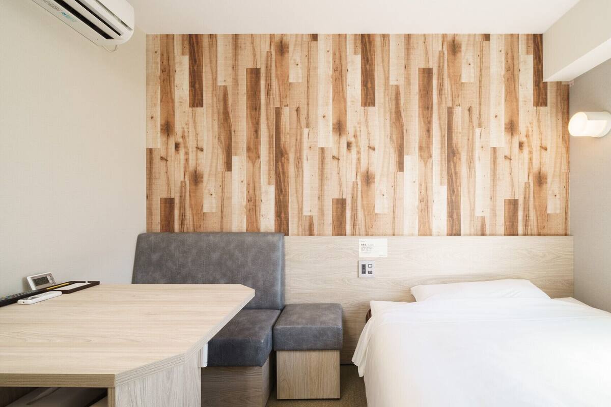 Une chambre d’hôtel avec un mur lambrissé en bois, un lit, un bureau et un canapé gris.