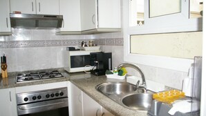 Una cocina con gabinetes blancos, estufa a gas, cafetera y pileta.
