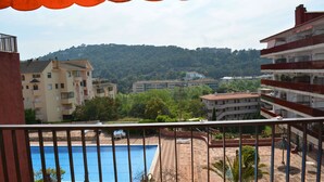 Vista de una piscina rodeada de edificios, con un paisaje montañoso al fondo.