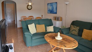 Una sala de estar con un sofá verde, una mesa de centro de madera y un televisor.