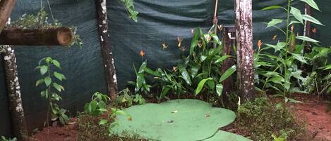 A garden with a green pathway, trees, and a green tarp-covered wall.