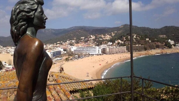 A statue overlooking a beach with buildings in the background. - Apartamento Voramar (Tossa de Mar)