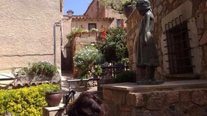 A courtyard with a statue, stone buildings, and potted plants. - Apartamento Voramar (Tossa de Mar)