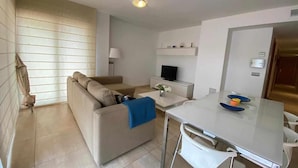 A modern living room with a sofa, a TV, a dining table, and a kitchen area. - Apartamento Voramar (Tossa de Mar)