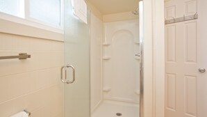Un bagno con box doccia in vetro, porta carta igienica e porta bianca.