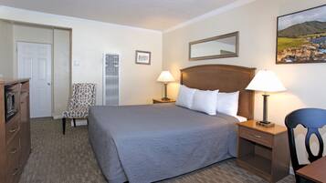 Quarto de hotel com uma cama grande, duas mesas de cabeceira com abajures, uma cadeira, cômoda e uma porta.