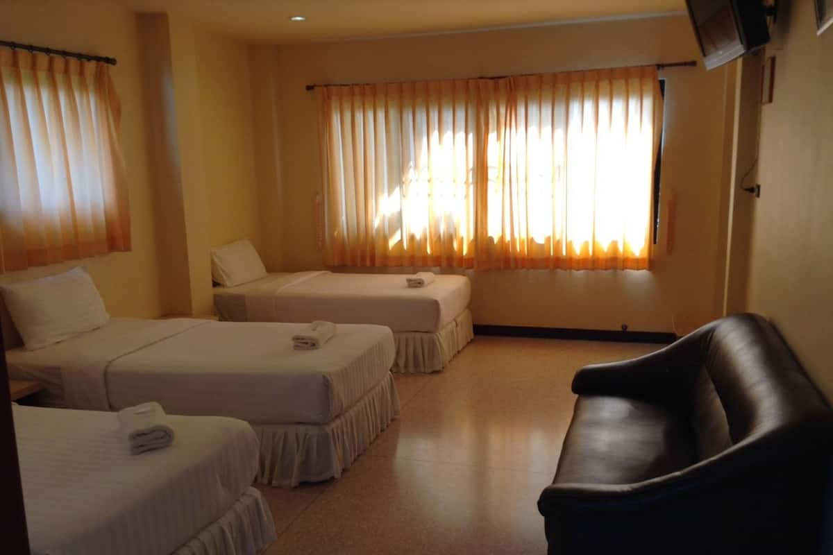 A hotel room with two single beds, a sofa, and large windows with curtains.