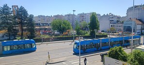 A tram station with blue trams, a clear sky, and urban buildings in the background. - Rooms Madison (Zagreb)