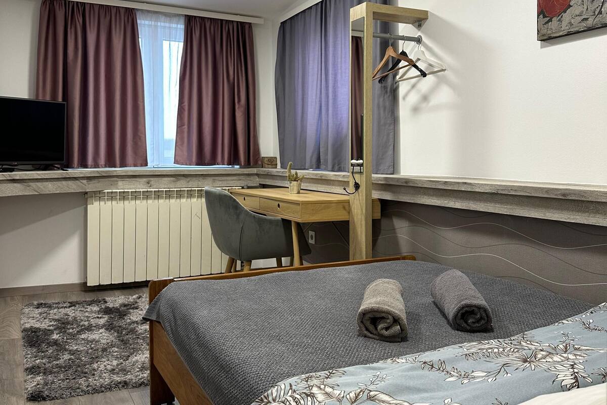 A bedroom with a bed, a desk, a chair, an air conditioner, and a painting on the wall.