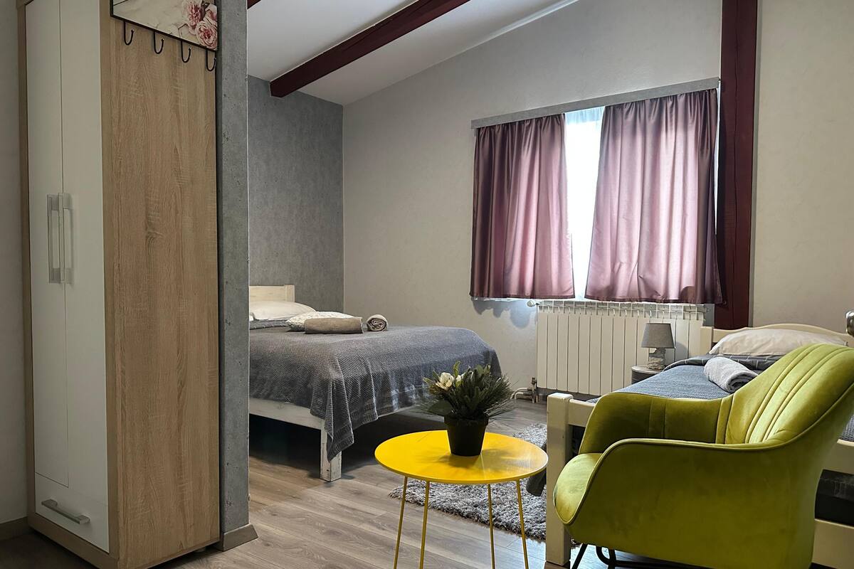 A bedroom with a bed, a green armchair, a small yellow table, and a radiator.