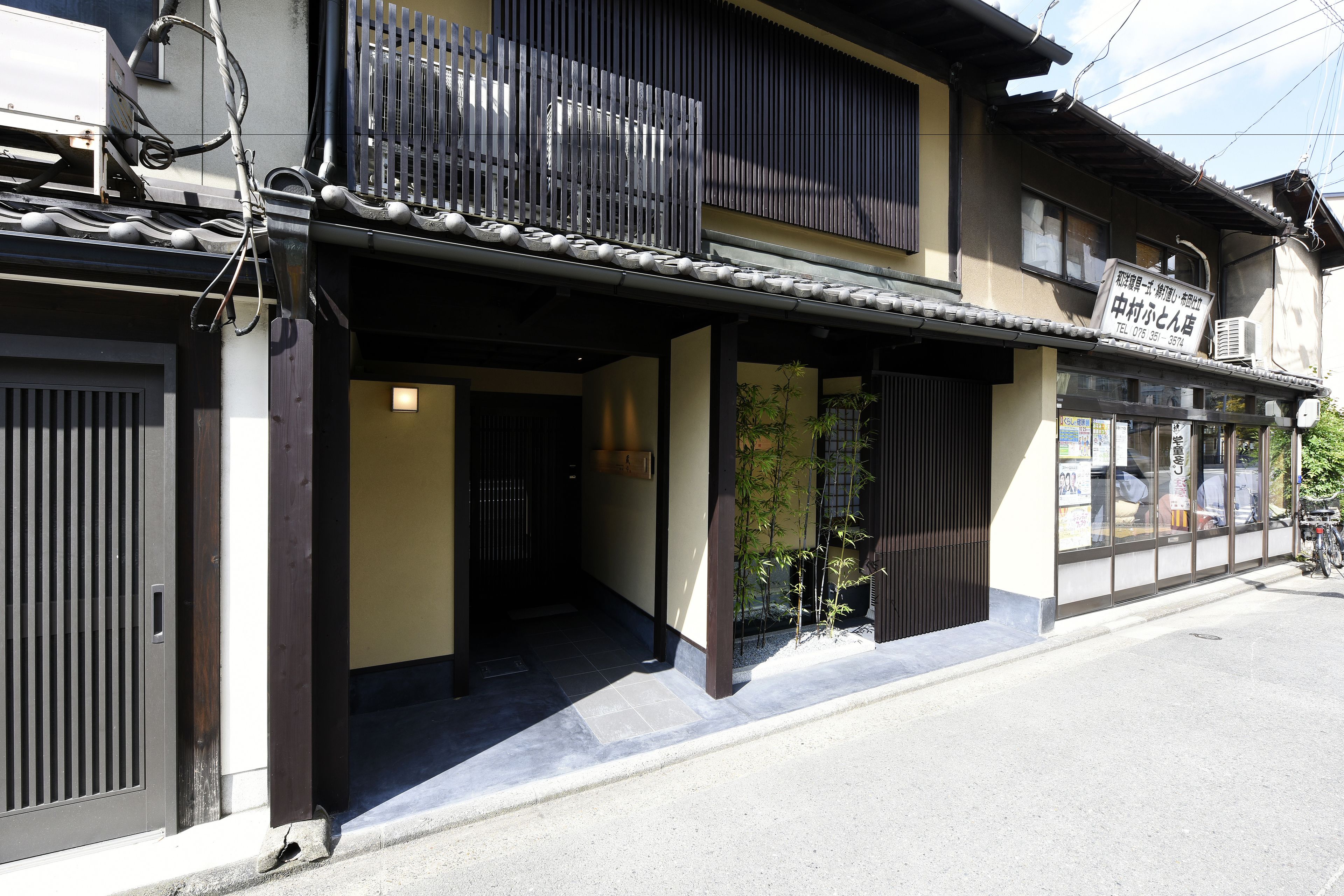 A traditional Japanese building with a wooden entrance, a small garden, and a signboard.