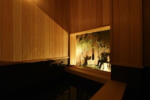 A room with wooden paneling, a small table, and a window with a view of a tree and a statue. - Kuraya Omiya-Shimabara (Kyoto)