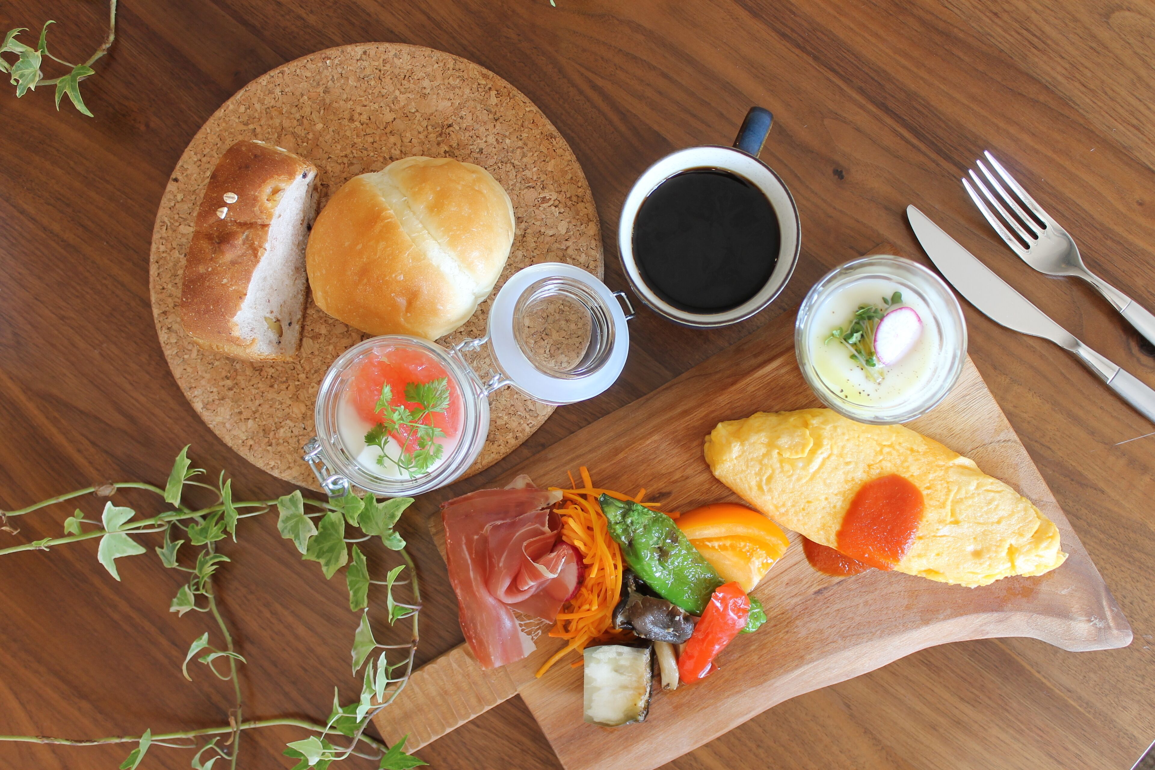 Ein Holztisch mit verschiedenen Speisen darunter Brot, eine Tasse Kaffee, ein Messer, eine Gabel und ein Teller mit Gemüse und Fleisch.