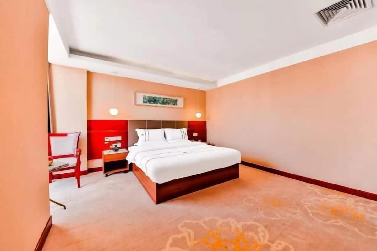 Hotellihuone, jossa on sänky, yöpöytä, tuoli ja taulu seinällä.
