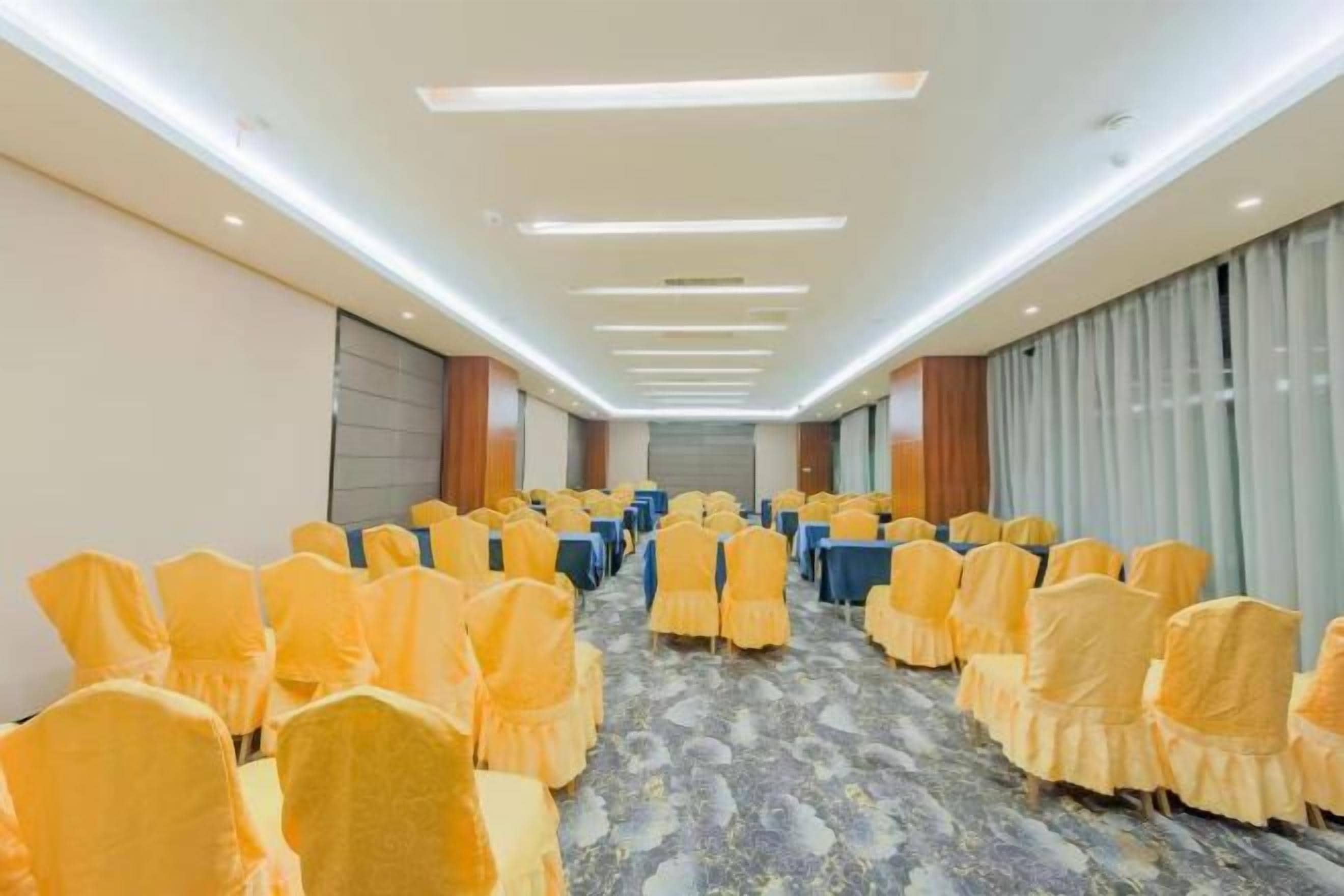 A conference room with rows of chairs and tables, a carpeted floor, and a long table at the front.