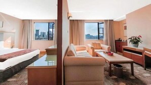 A hotel room with a bed, sofa, dining table, and a view of the cityscape. - Camellia Hotel (Kunming)