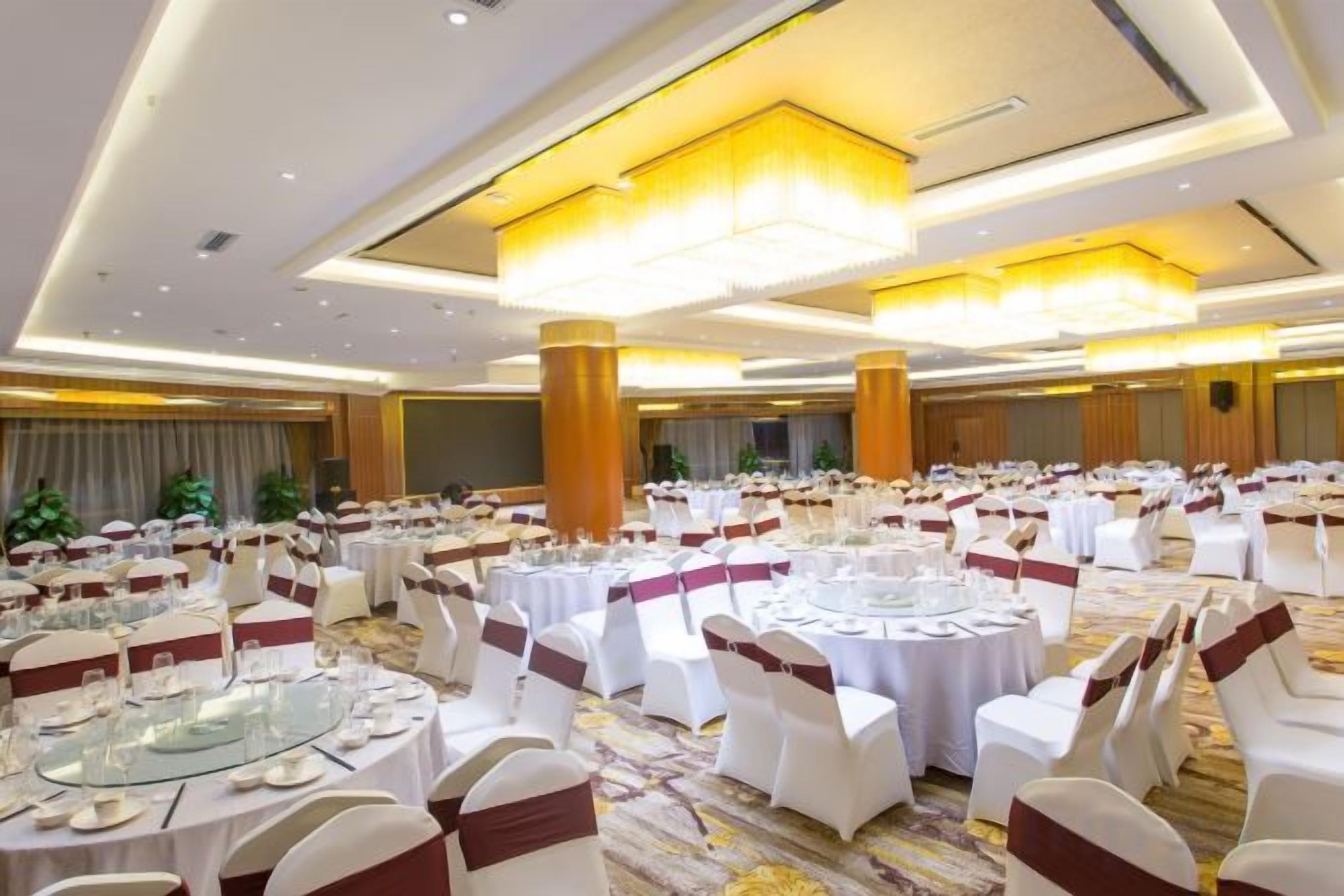 Een feestzaal met ronde tafels, witte stoelen en een vloerbedekking.